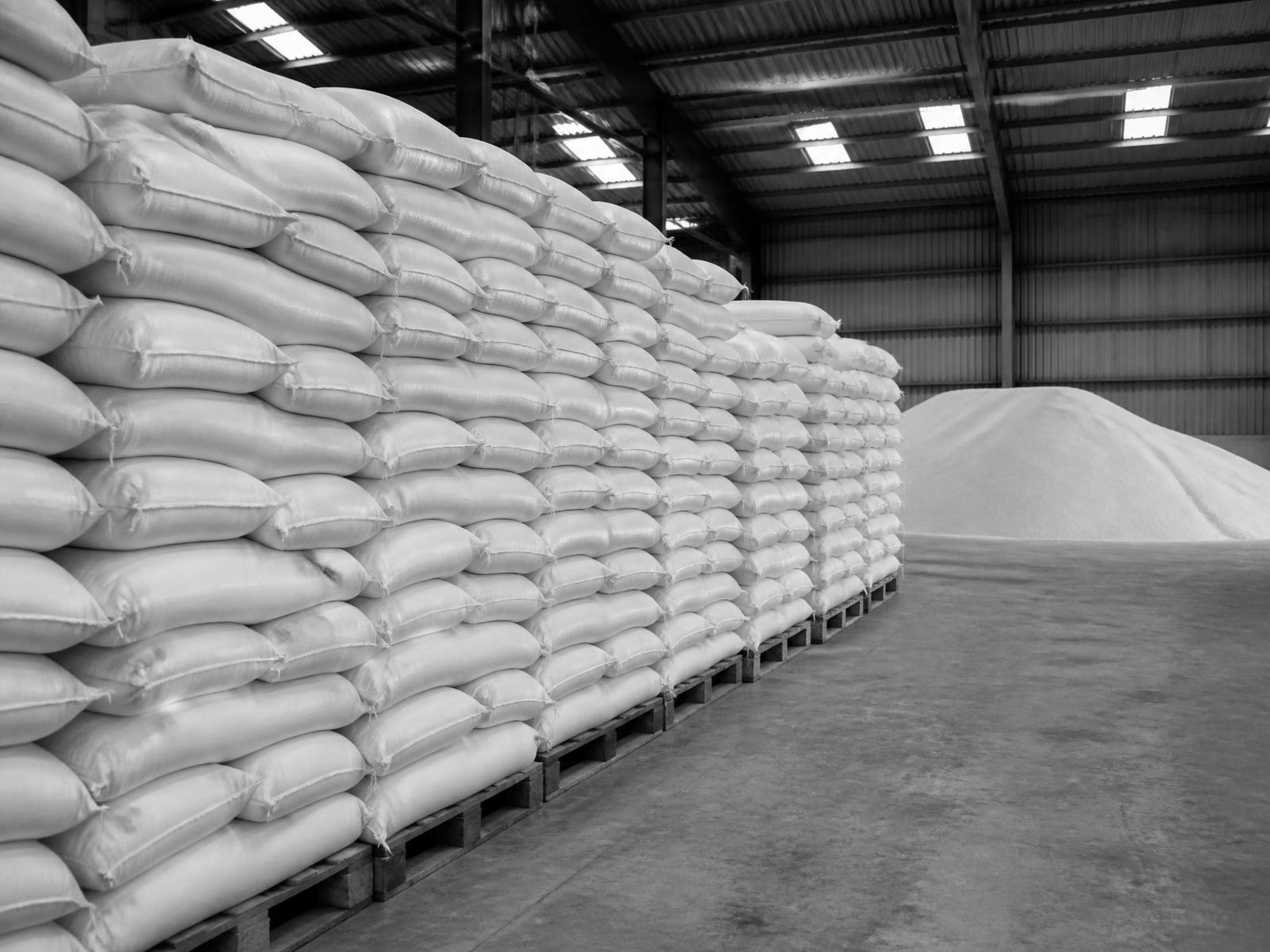 Monochrome photograph of bagged sugar stacked on pallets in warehouse storage